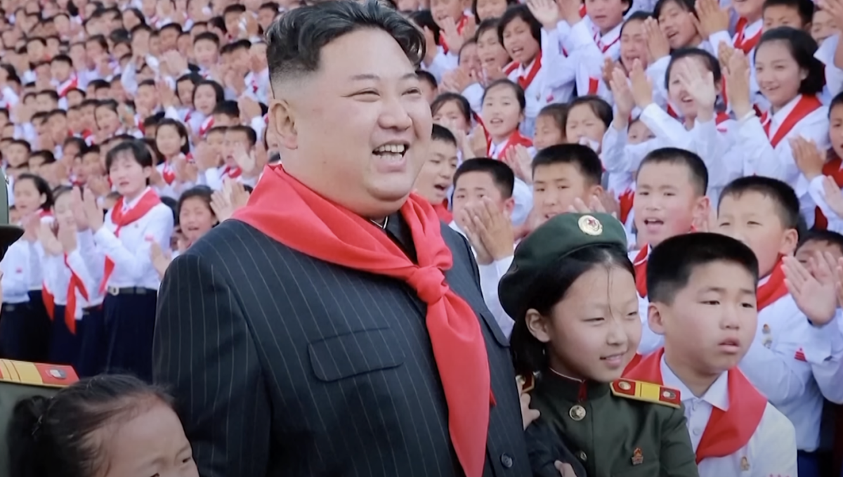 Kim smiling, standing beside a group of schoolchildren.